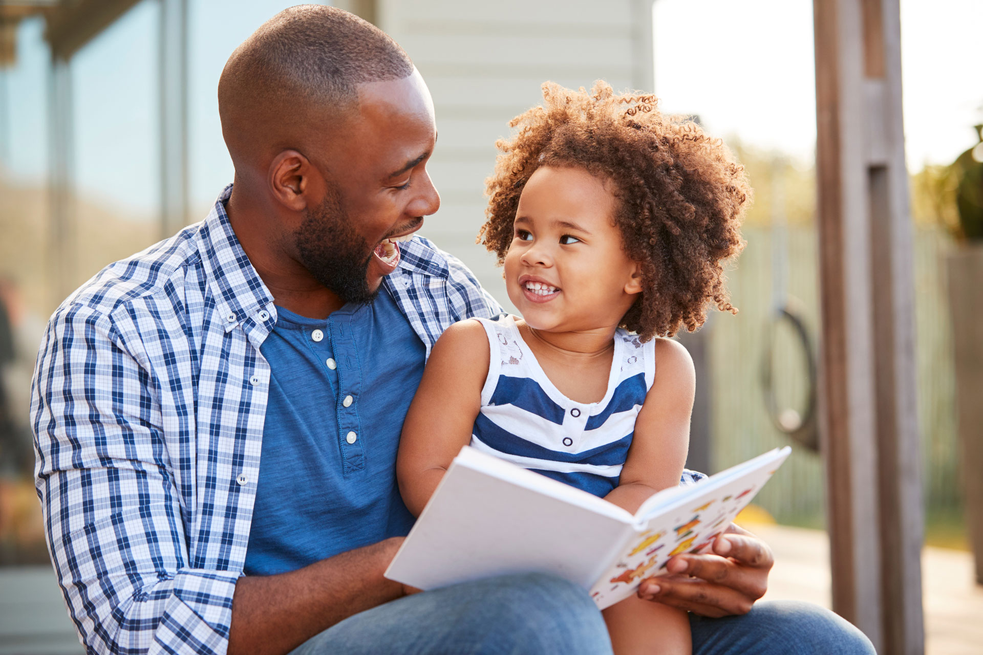 Young black father and daughter reading book outside